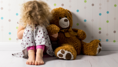 دختر بچه ای نشسته کنار عروسک خرسش و زانو هاشو بغل کرده | پیشگیری از آزار جنسی کودک