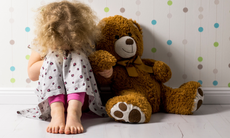دختر بچه ای نشسته کنار عروسک خرسش و زانو هاشو بغل کرده | پیشگیری از آزار جنسی کودک